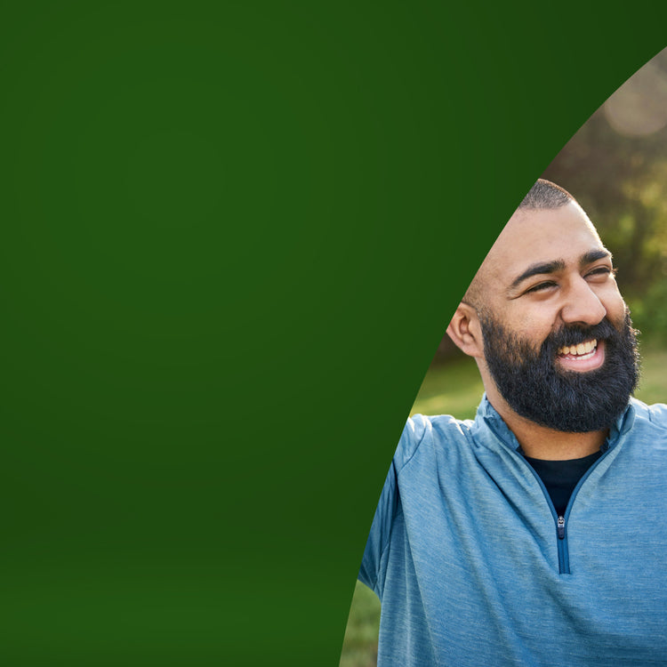 A smiling man with a beard wearing a heather blue quarter-zip pullover shirt, partially visible on the right side of the frame with a large green graphic shape on the left.- mobile